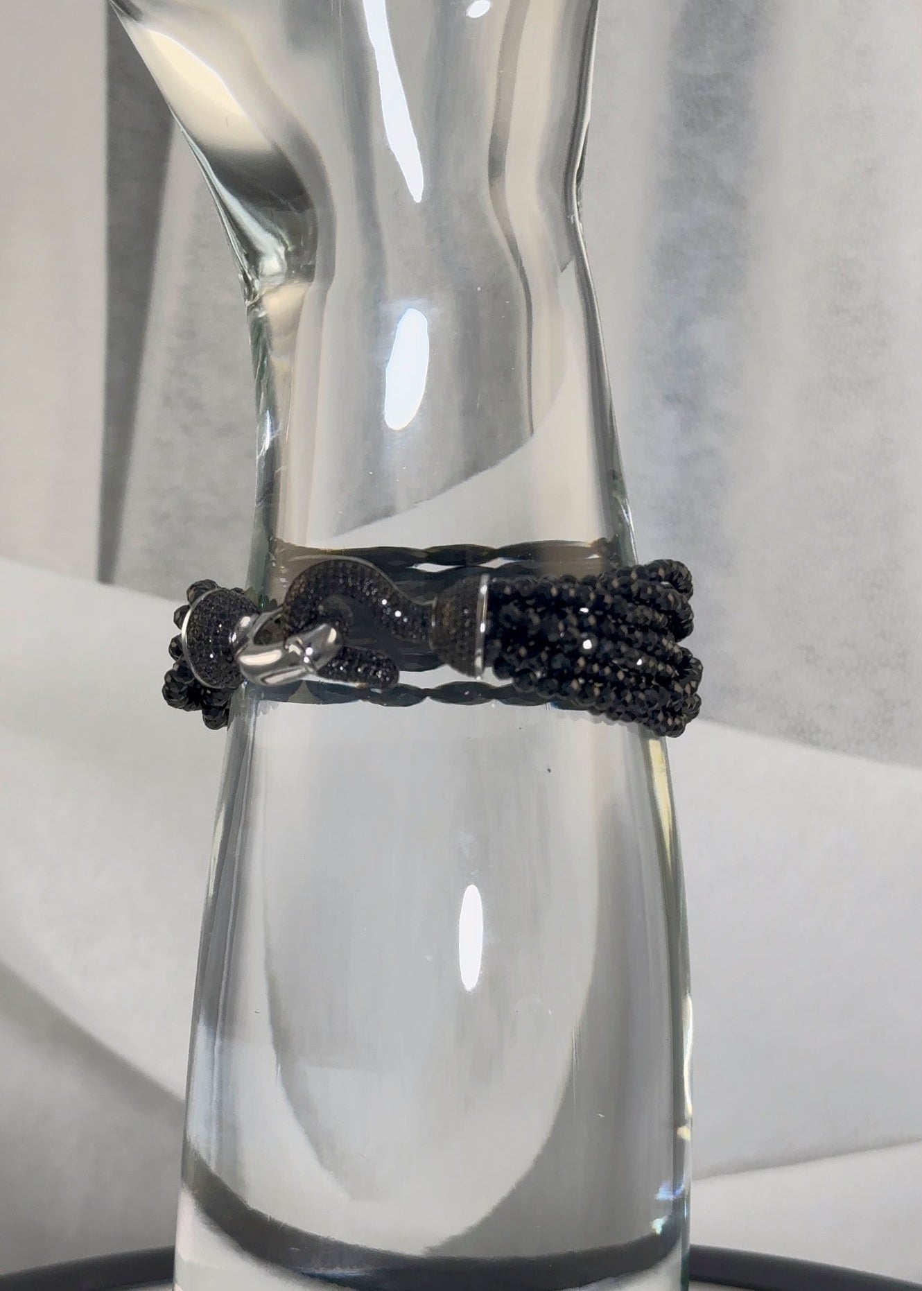 Clear glass display with a black beaded bracelet , black hook clasp, around its middle on a white background