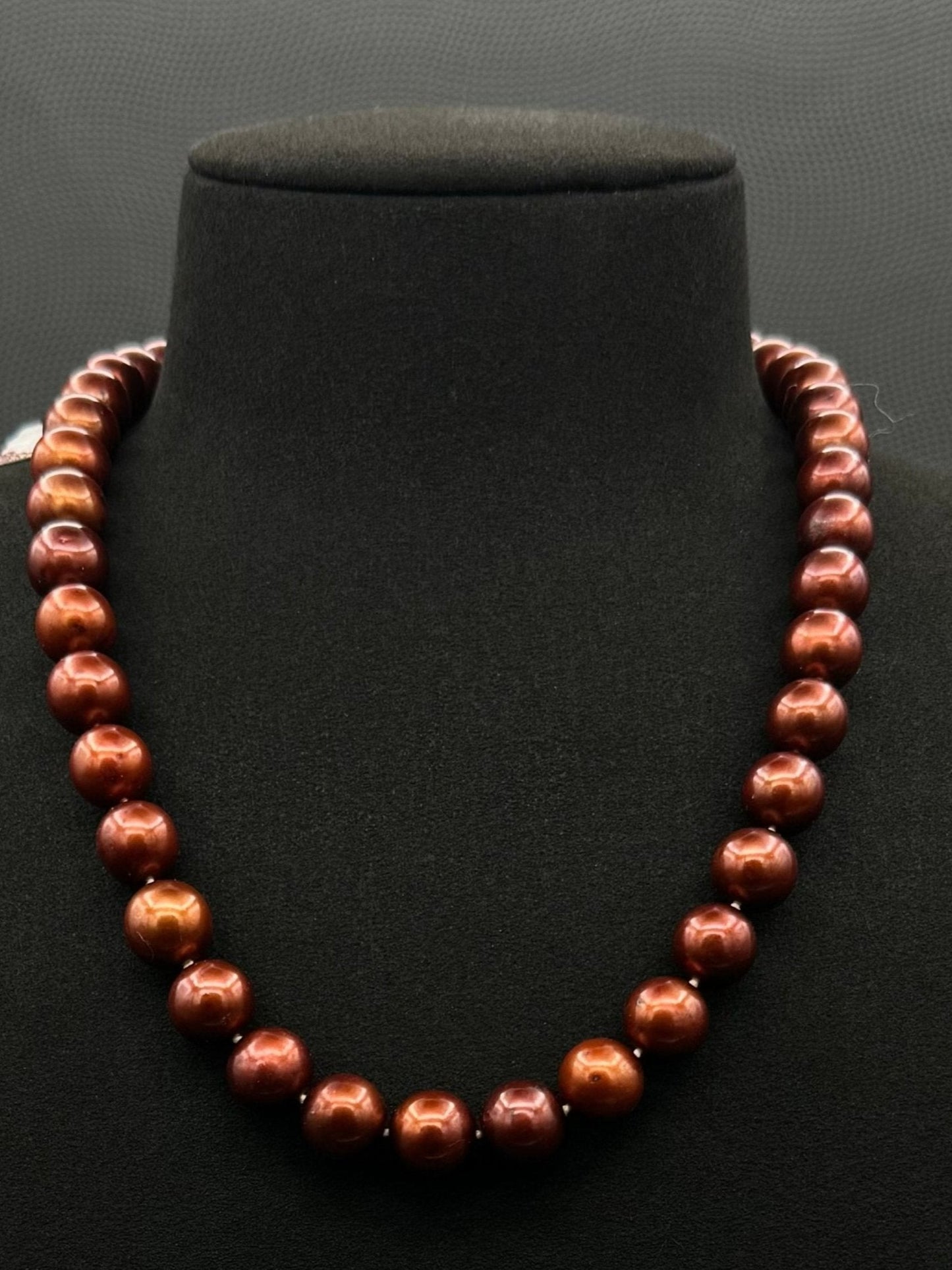Cultured, Tahitian russet-brown pearl strand necklace, exhibited on black suede, excellent reflection, 10.5-11mm, 18", yellow gold clasp.