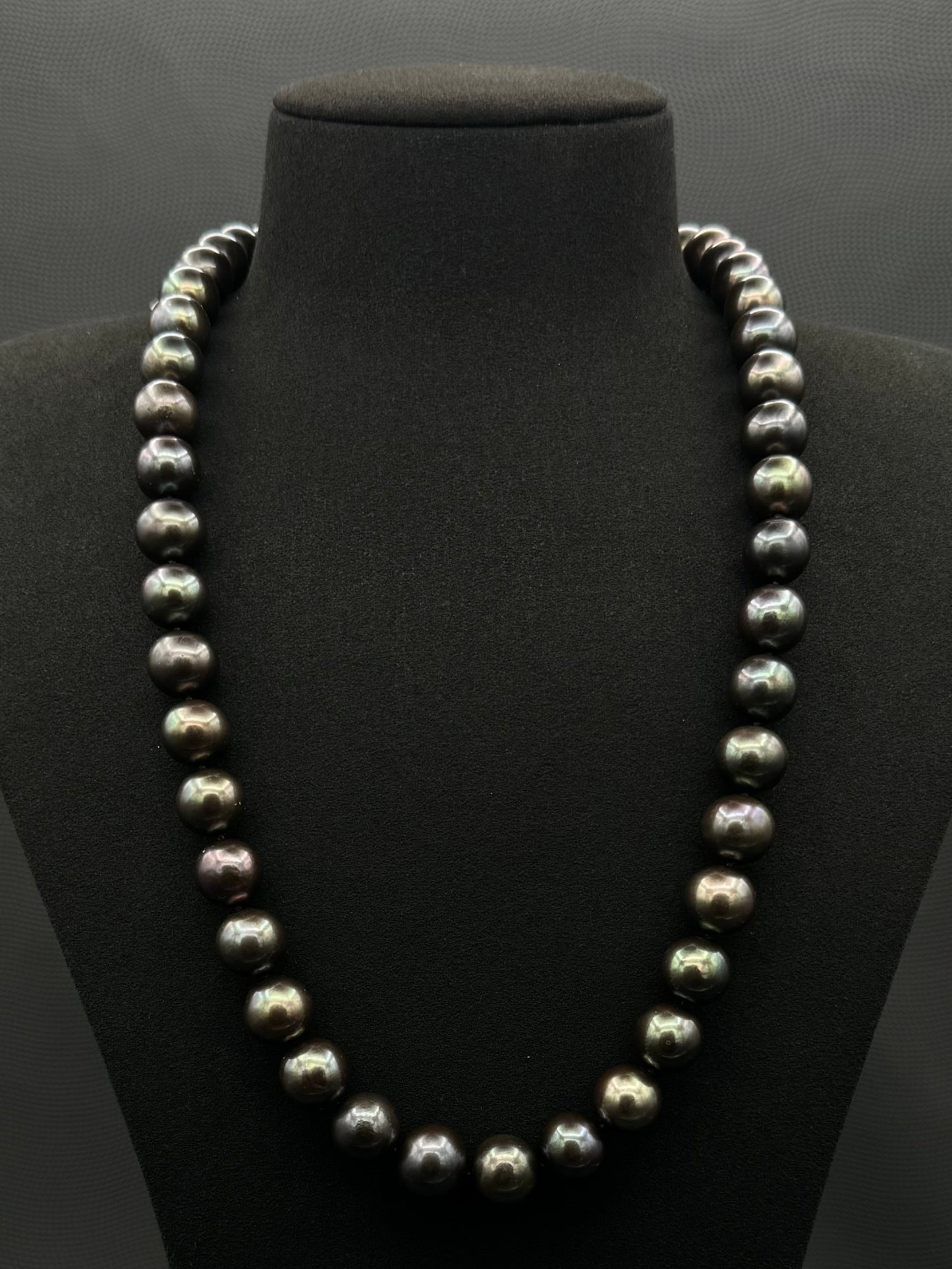 Cultured, Tahitian black-green continuous strand pearl necklace, exhibited on black suede, excellent reflection, 11.5-12.5mm, 24", no clasp.